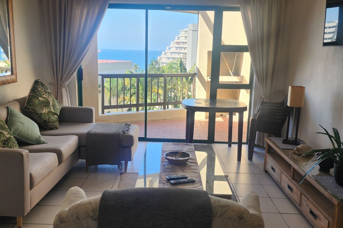 A comfortable living room featuring tiled flooring and a large sliding glass door that opens onto a balcony with scenic coastal views.