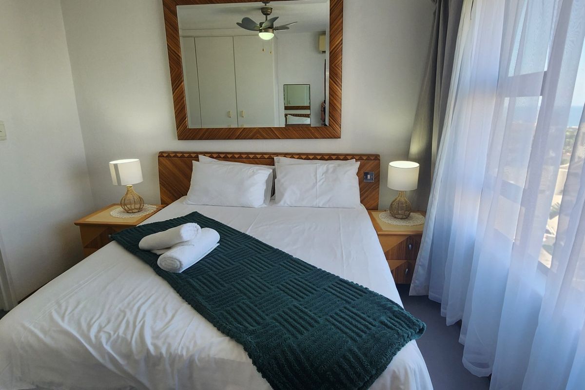 A well-maintained bedroom featuring built-in cupboards, a ceiling fan, and an attached en-suite bathroom with natural light from the adjacent window.