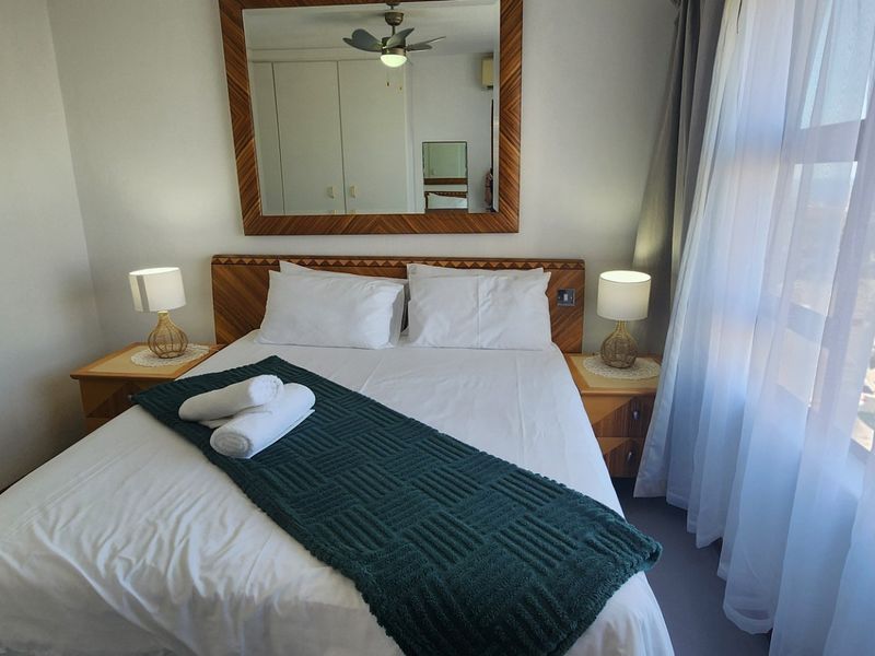 A well-maintained bedroom featuring built-in cupboards, a ceiling fan, and an attached en-suite bathroom with natural light from the adjacent window.