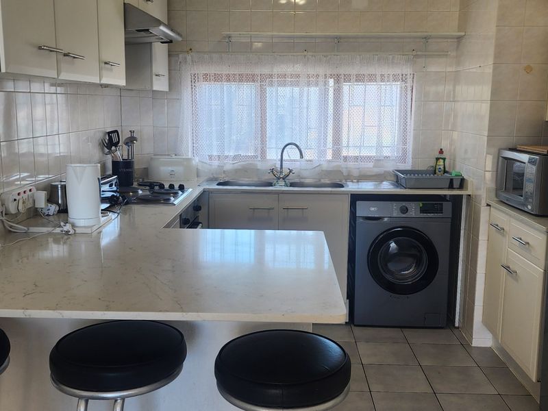 Functional kitchen featuring stone countertops, built-in cabinetry, tiled backsplash, gas hob, extractor fan, and dedicated space for a washing machine.