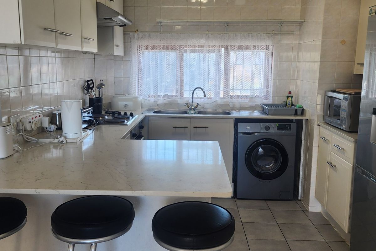 Functional kitchen featuring stone countertops, built-in cabinetry, tiled backsplash, gas hob, extractor fan, and dedicated space for a washing machine.