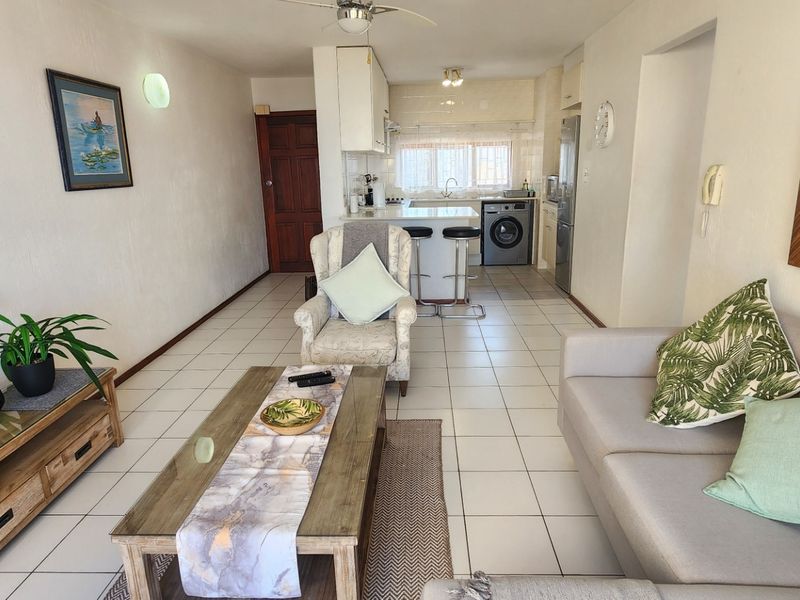 Open-plan living area featuring tiled flooring, a ceiling fan, and a functional kitchen space with integrated laundry connections.