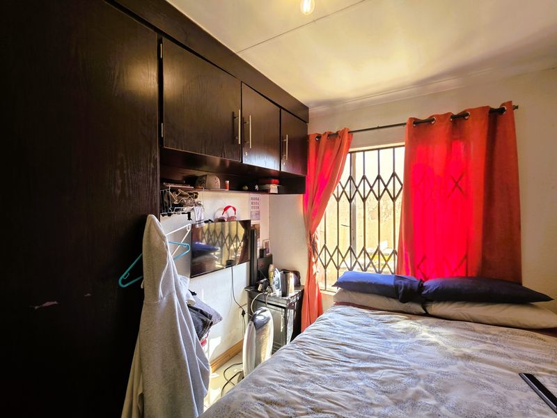 A compact bedroom featuring built-in dark wood cabinetry and a window fitted with a security gate.