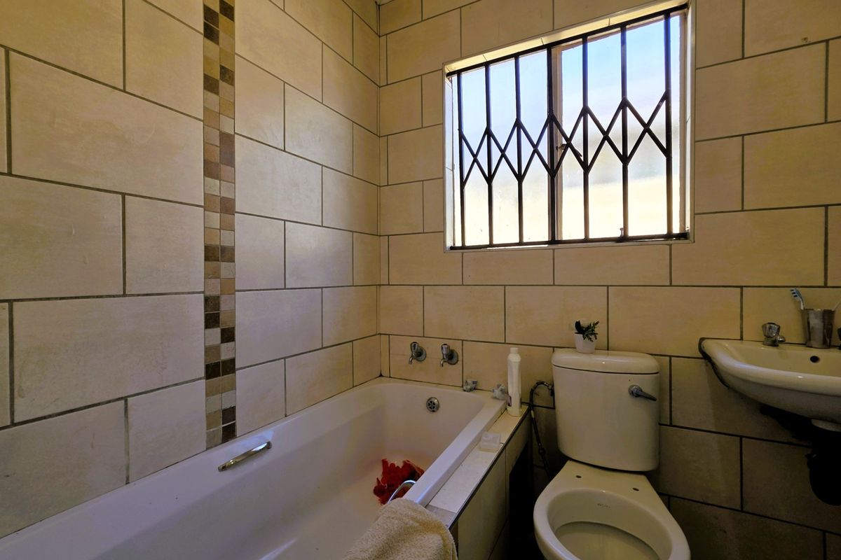 A functional bathroom featuring a bathtub, toilet, and washbasin with tiled walls and a window fitted with a security gate.