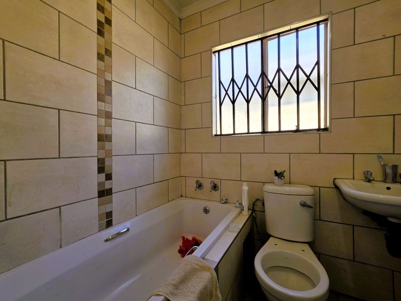 A functional bathroom featuring a bathtub, toilet, and washbasin with tiled walls and a window fitted with a security gate.