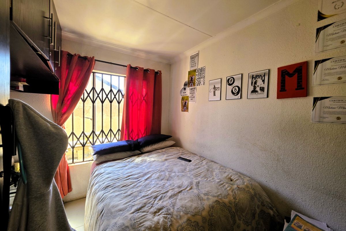 A compact bedroom featuring built-in cabinetry, a security gate on the window, and standard ceiling finishes.