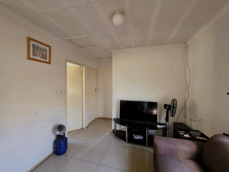 A living room area featuring tiled flooring and internal access doors, currently showing signs of wear including stained walls and visible wiring.