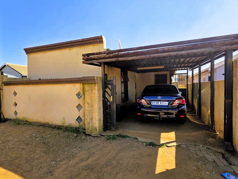 Front exterior view of the property featuring a covered carport, boundary wall with decorative inserts, and a gated entrance.