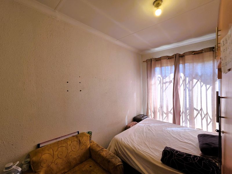 A compact bedroom featuring a security gate over the window and visible wall damage from previously mounted fixtures.