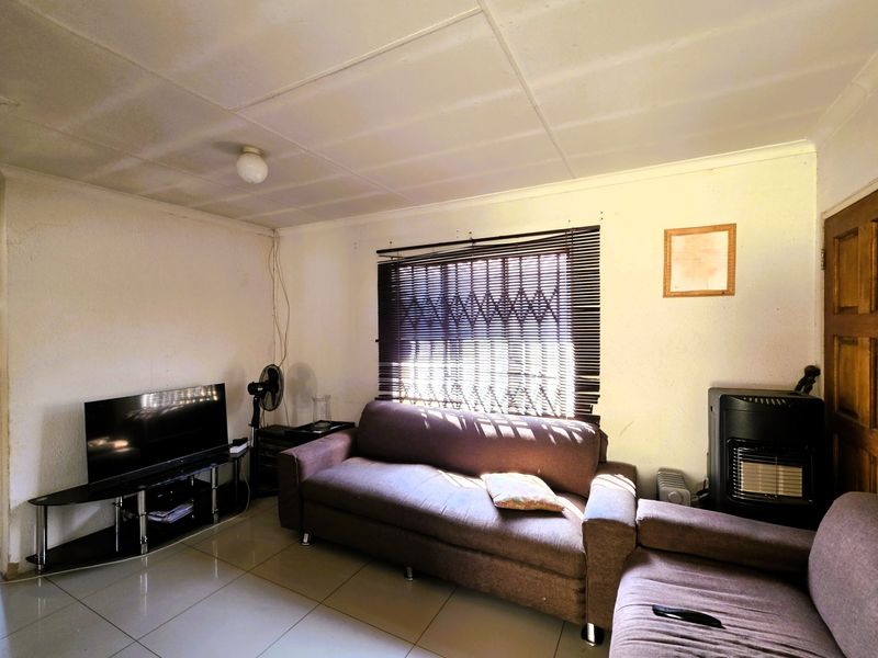 A living room featuring tiled flooring, a built-in gas heater, and security window treatments, requiring cosmetic updates to improve the overall aesthetic.