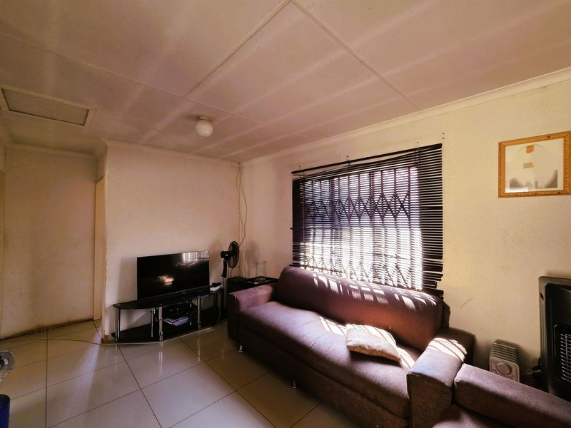 A living room featuring tiled flooring, security gate on the window, and venetian blinds, offering a functional space with potential for cosmetic updates.
