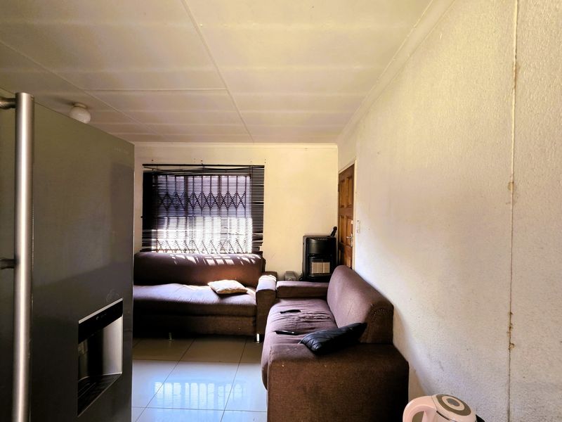 A living room area featuring tiled flooring, a security gate on the window, and a timber door, requiring cosmetic updates to the walls and ceiling.