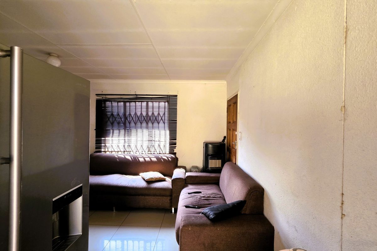 A living room area featuring tiled flooring, a security gate on the window, and a timber door, requiring cosmetic updates to the walls and ceiling.