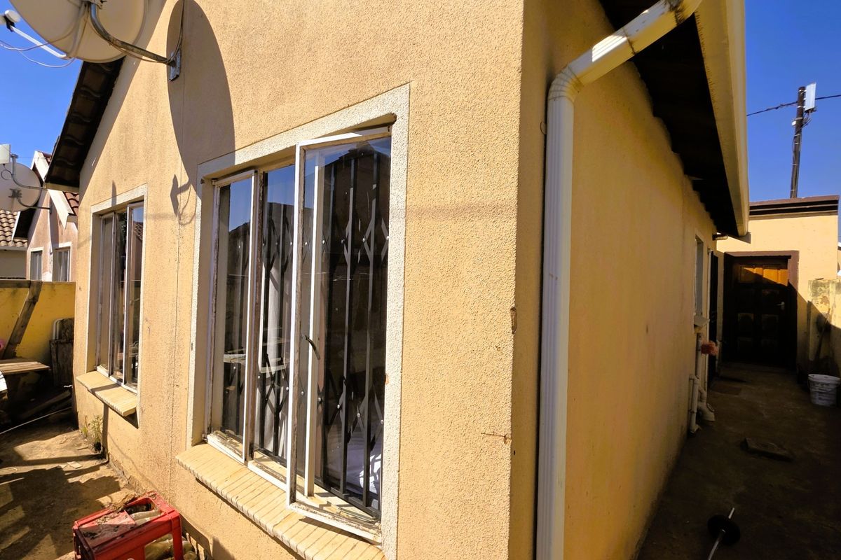 A side view of the property showing exterior plastered walls, security gates on windows, and functional rainwater drainage systems.