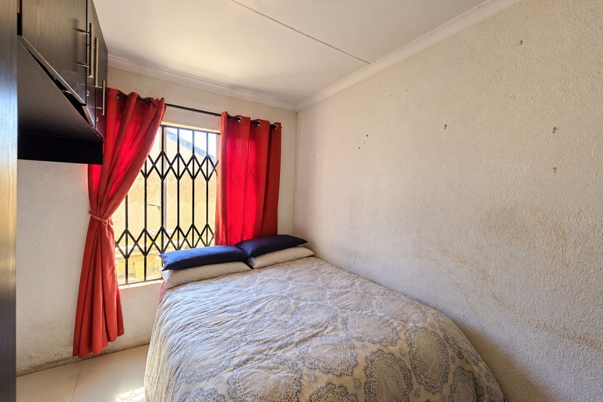 A compact bedroom featuring tiled flooring, built-in cabinetry, and a security gate on the window, requiring cosmetic wall repairs.