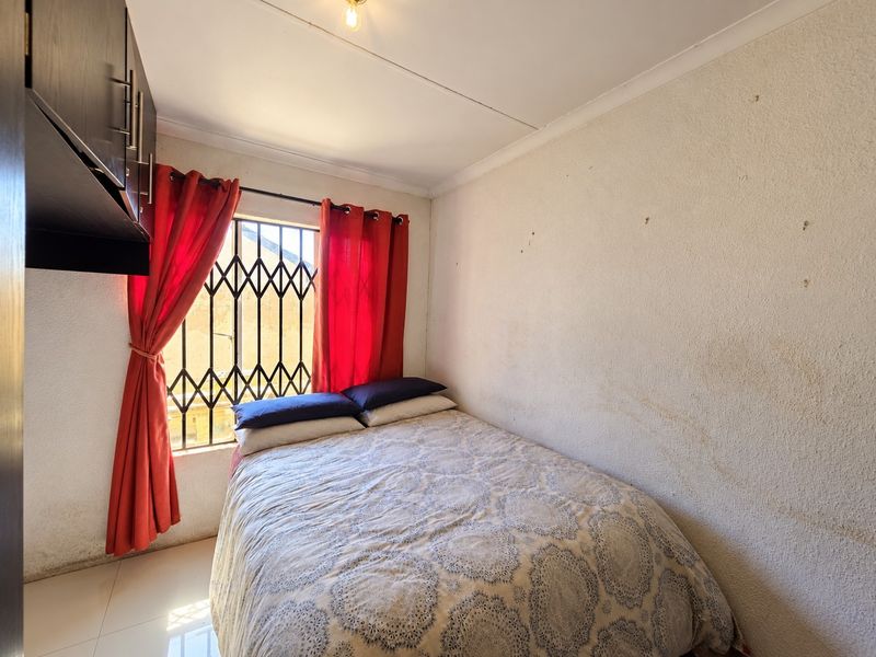 A compact bedroom featuring tiled flooring, built-in cabinetry, and a security gate on the window, requiring cosmetic wall repairs.