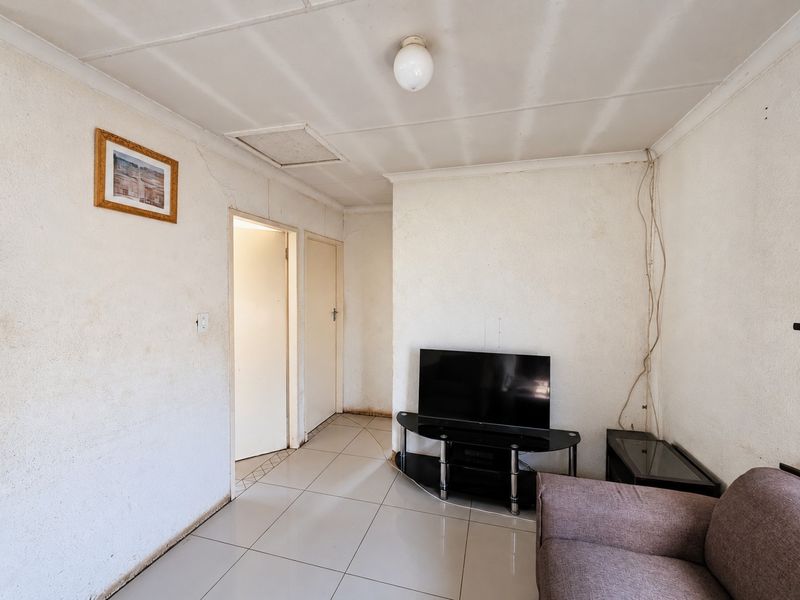 A living room featuring tiled flooring and a ceiling access hatch, currently showing signs of wear including stained walls and exposed wiring.