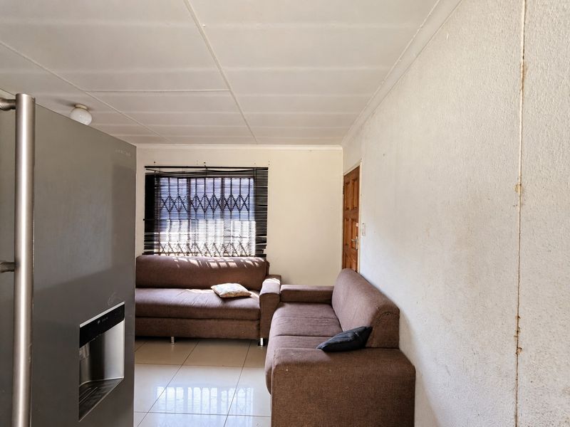 A living area featuring tiled flooring, security window treatments, and a timber door, requiring cosmetic updates to the wall finishes.