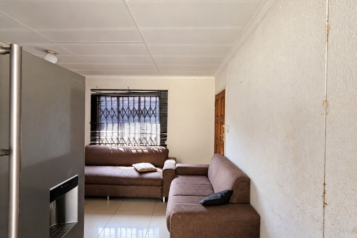 A living area featuring tiled flooring, security window treatments, and a timber door, requiring cosmetic updates to the wall finishes.