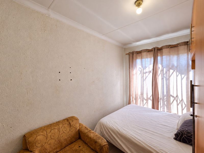 A compact bedroom featuring a built-in wardrobe, security gate on the window, and textured wall finishes requiring minor repair.