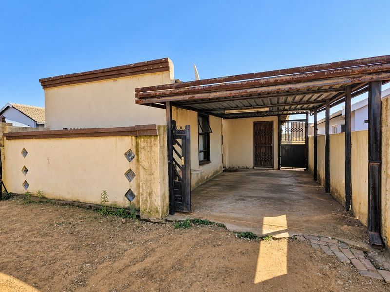 Front exterior view featuring a covered carport, concrete driveway, and perimeter boundary wall with security gate access.