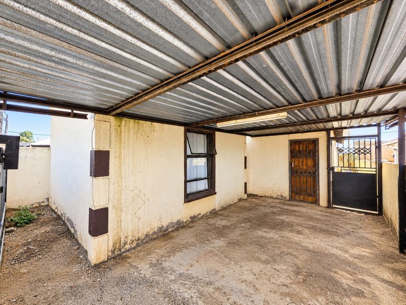 A covered outdoor parking area or garage space featuring a corrugated metal roof, concrete flooring, and security gates.