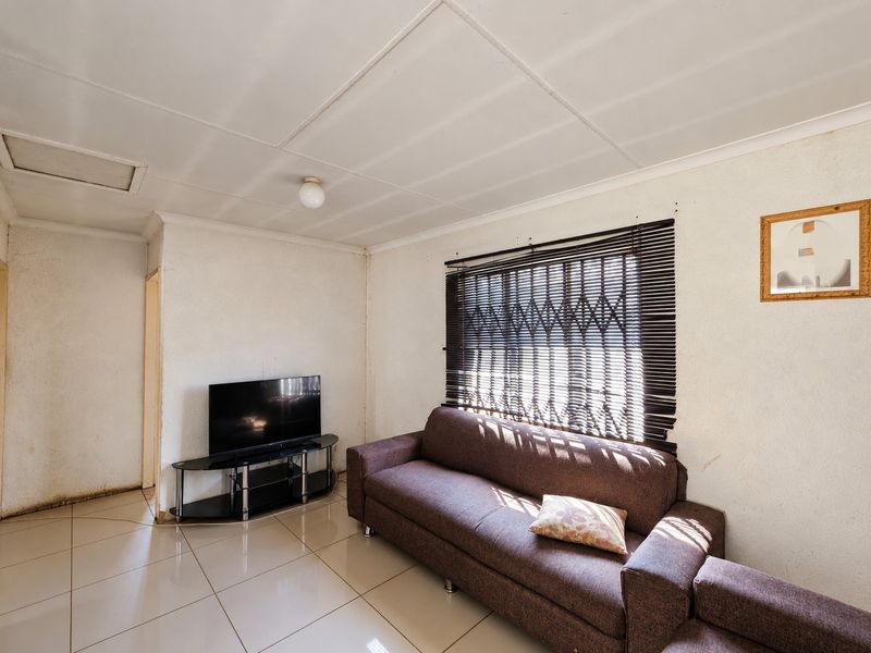 A living room featuring tiled flooring, a security gate on the window, and a standard ceiling finish.