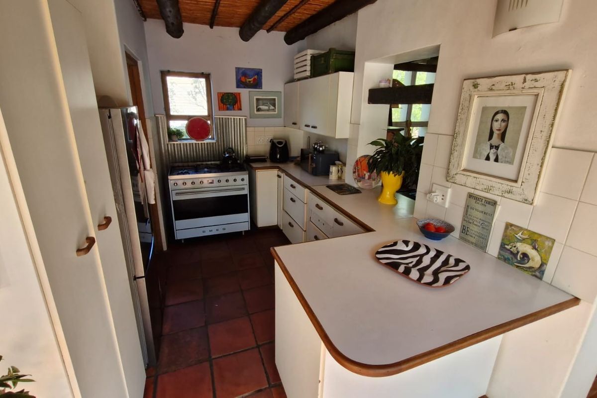 A rustic kitchen featuring exposed timber beam ceilings, tiled flooring, white cabinetry, and a gas stove with a metal backsplash.