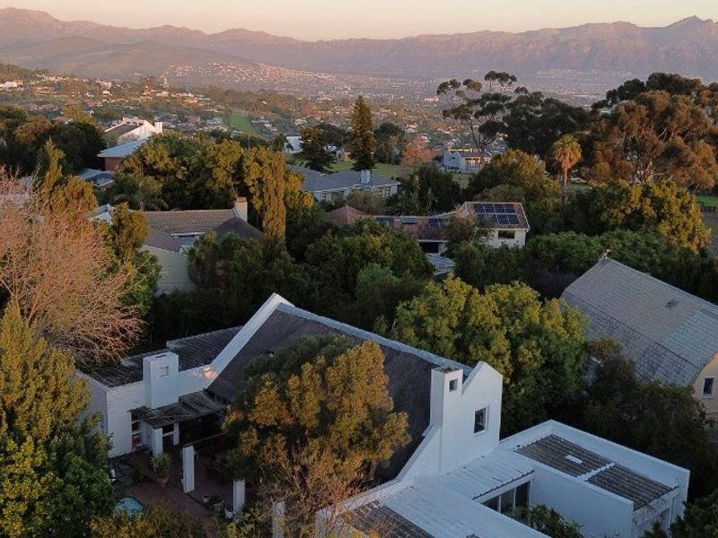 Aerial view of a residential property featuring a white exterior, tiled roof with solar panels, paved driveway, and scenic mountain views.