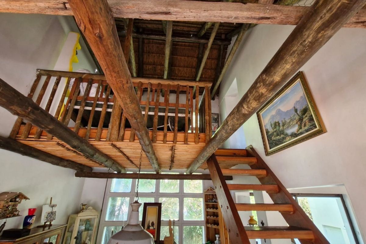 Living area featuring a double-volume space with exposed timber beams, a thatched roof, a mezzanine level, and a timber staircase.