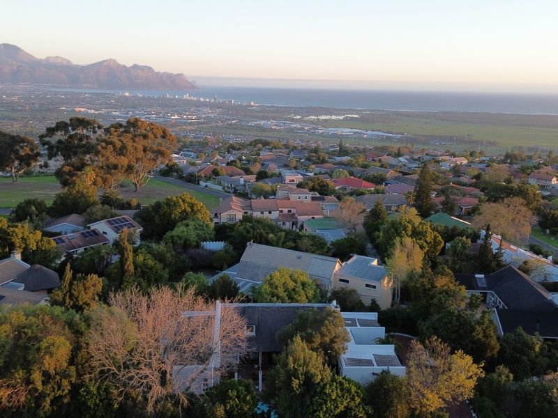 An elevated aerial view showcasing the surrounding residential neighbourhood, coastal landscape, and distant mountain range.