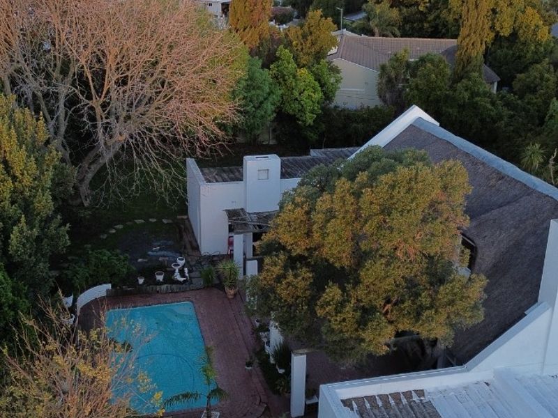 Aerial view of a residential property featuring a swimming pool, brick patio, and a thatched roof, set against a scenic mountain backdrop.