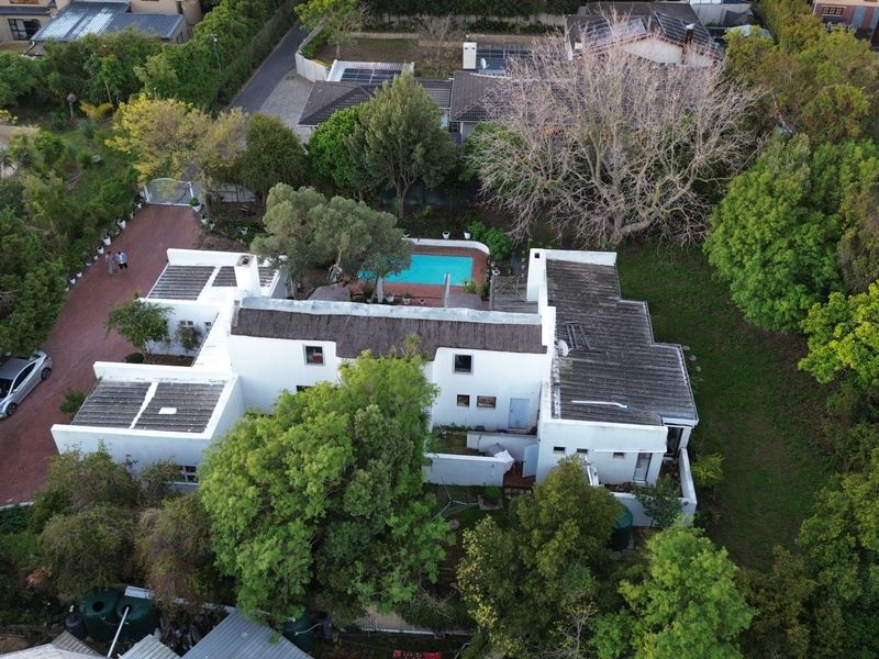 Aerial view of the property showcasing the main dwelling, swimming pool, surrounding garden, and paved driveway area.