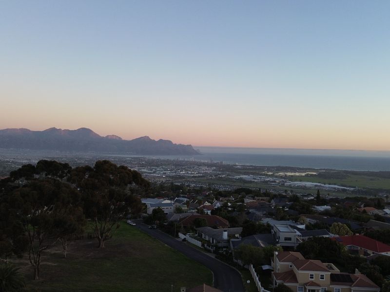 An elevated aerial view showcasing the surrounding landscape, coastline, and mountain range at sunset.