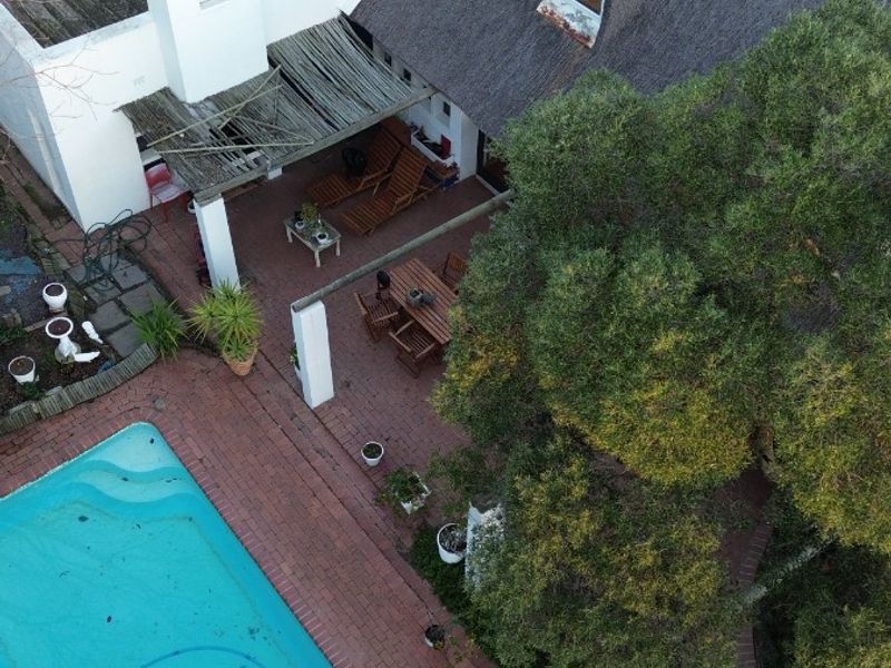 Aerial view of a property featuring a swimming pool, brick-paved patio area, and a traditional thatched roof structure.
