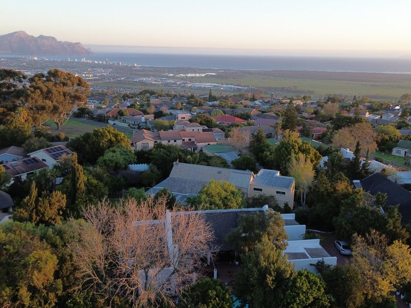 An elevated aerial view of the residential property and surrounding neighbourhood, showcasing the coastal landscape and mountain backdrop.