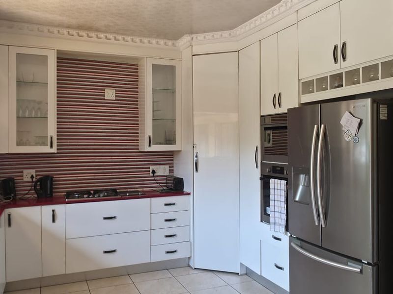 A functional kitchen featuring white cabinetry, a gas hob, built-in oven, and a double sink with tiled flooring and decorative crown molding.