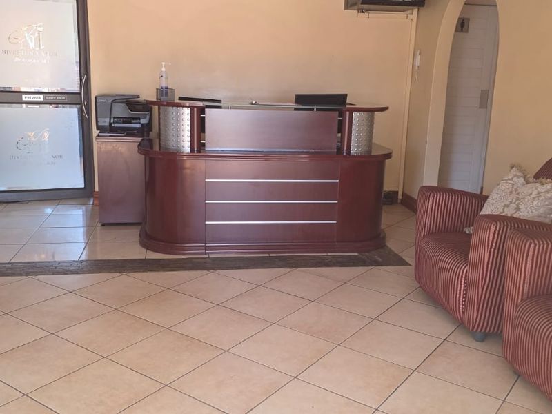 A functional guest house reception area featuring a built-in wooden reception desk, tiled flooring, and a glass entrance door.
