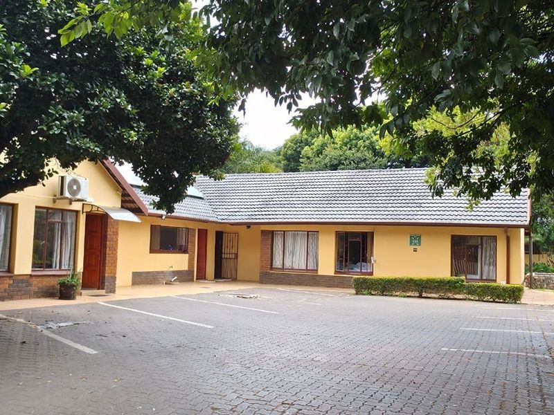 Front exterior view of the guest house featuring a paved parking area, brick and plaster facade, and established garden surroundings.