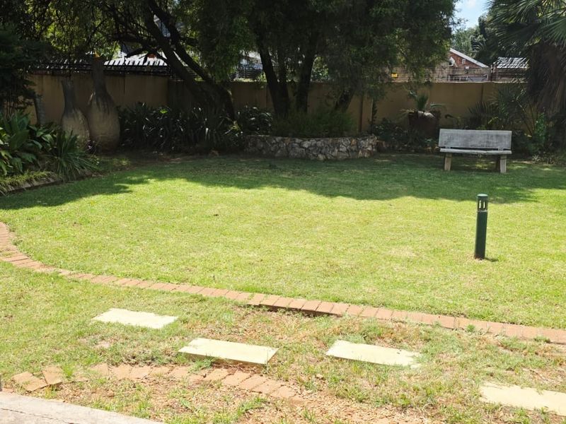 A landscaped garden area featuring a lawn, stone retaining wall, brick-edged pathways, and perimeter boundary walls.