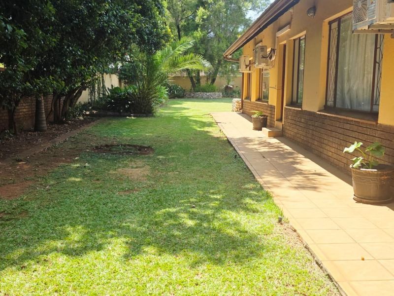 A view of the rear exterior of the guest house, featuring a tiled patio walkway, brick facade, and a spacious garden area.