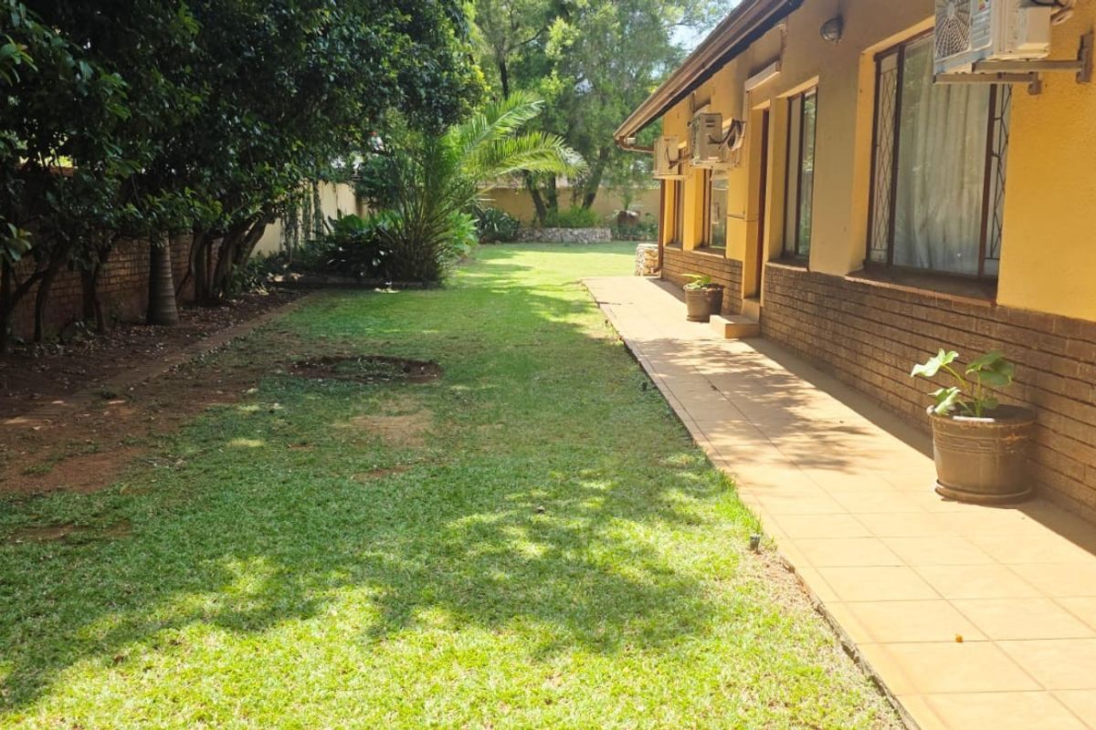 A view of the rear exterior of the guest house, featuring a tiled patio walkway, brick facade, and a spacious garden area.
