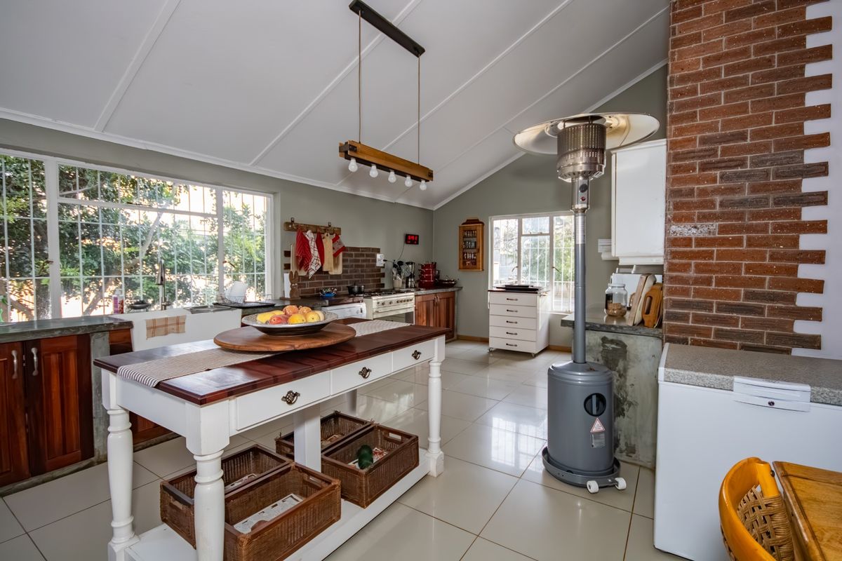 Spacious kitchen featuring vaulted ceilings, exposed brickwork, timber cabinetry, and large windows providing ample natural light.