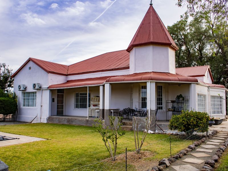 Rear view of a character home featuring a distinctive turret, corrugated metal roof, covered patio, and established garden with a stone pathway.