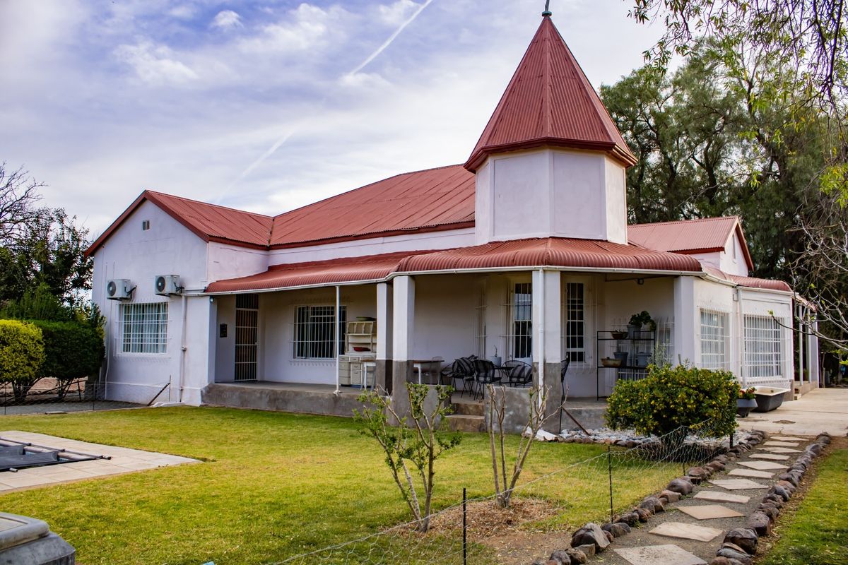 Rear view of a character home featuring a distinctive turret, corrugated metal roof, covered patio, and established garden with a stone pathway.