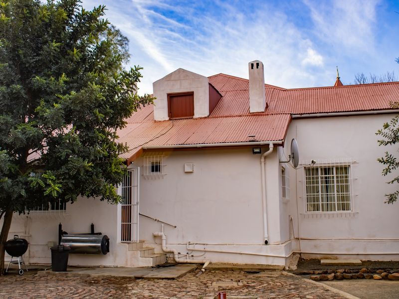 Rear view of the property featuring a corrugated metal roof, a dormer window, a chimney, and a paved courtyard area.