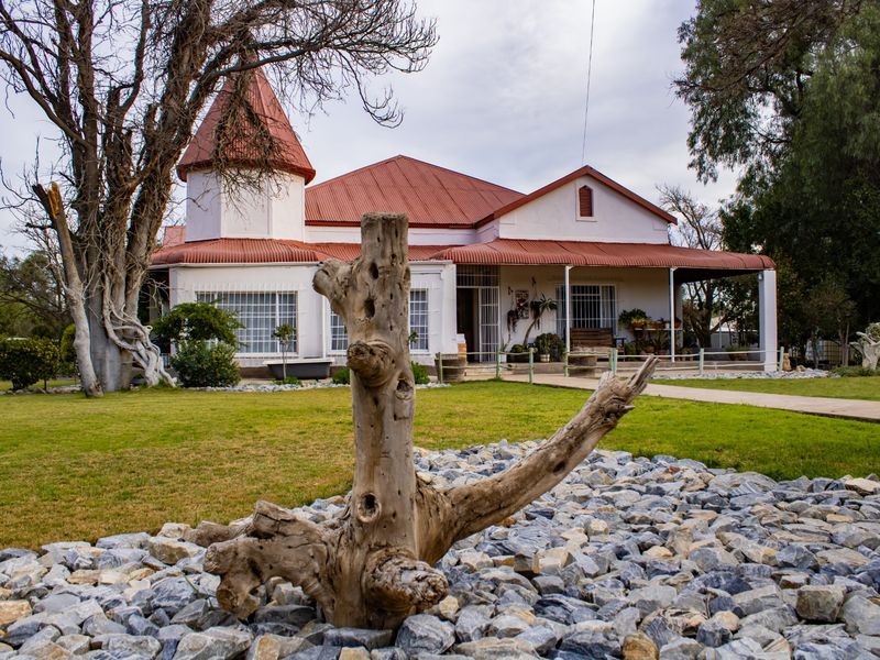 A charming single-story house featuring a distinctive turret, corrugated metal roof, and a spacious covered veranda overlooking a landscaped garden.