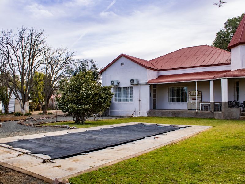 Rear view of the property featuring a swimming pool with a cover, a covered patio area, and established garden surroundings.