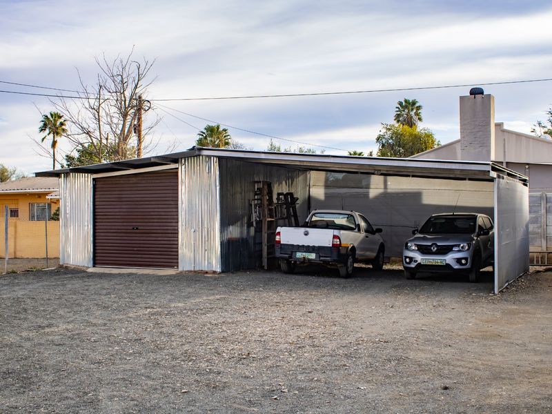 A functional garage and attached carport structure featuring corrugated metal siding and a roll-up door, situated on a gravel driveway.