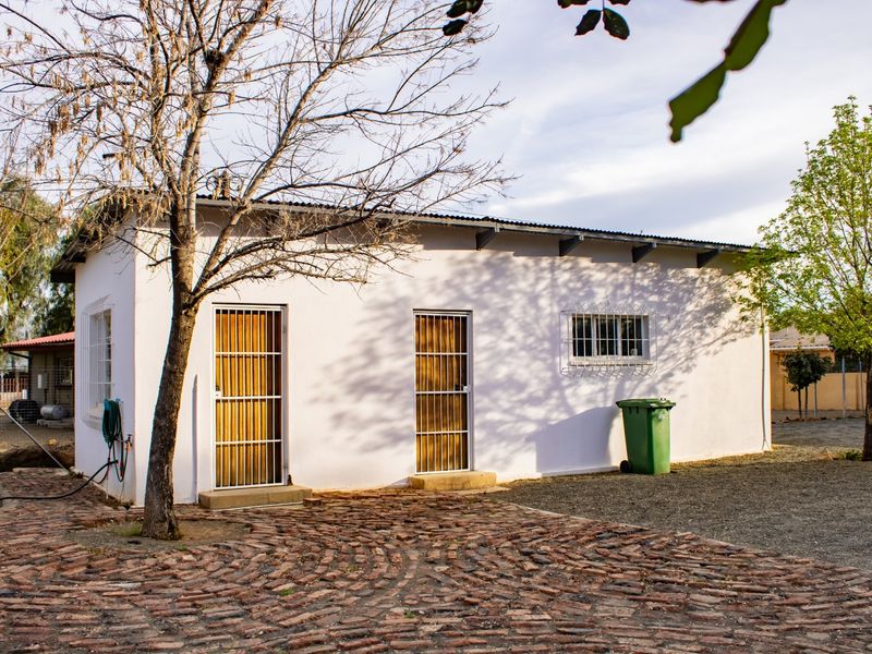 Rear view of a single-story dwelling featuring a corrugated metal roof, security-gated entrances, and a brick-paved courtyard area.